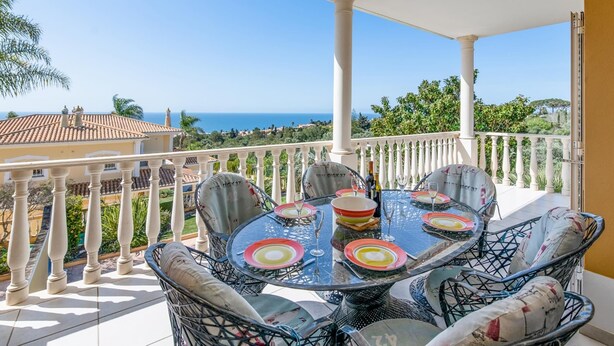 A balcony with a table set for dining, overlooking a scenic view of the sea and greenery. - Casa Mira Luz, villa with private pool (Praia da Luz)