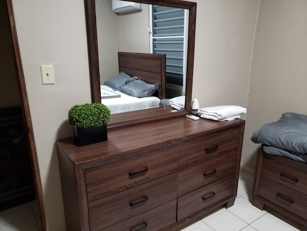 A wooden dresser with a mirror, a small potted plant, and a remote control. - Rent It (Aguadilla)