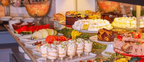 Un bufé con diversos platos, incluyendo postres, frutas y aperitivos.