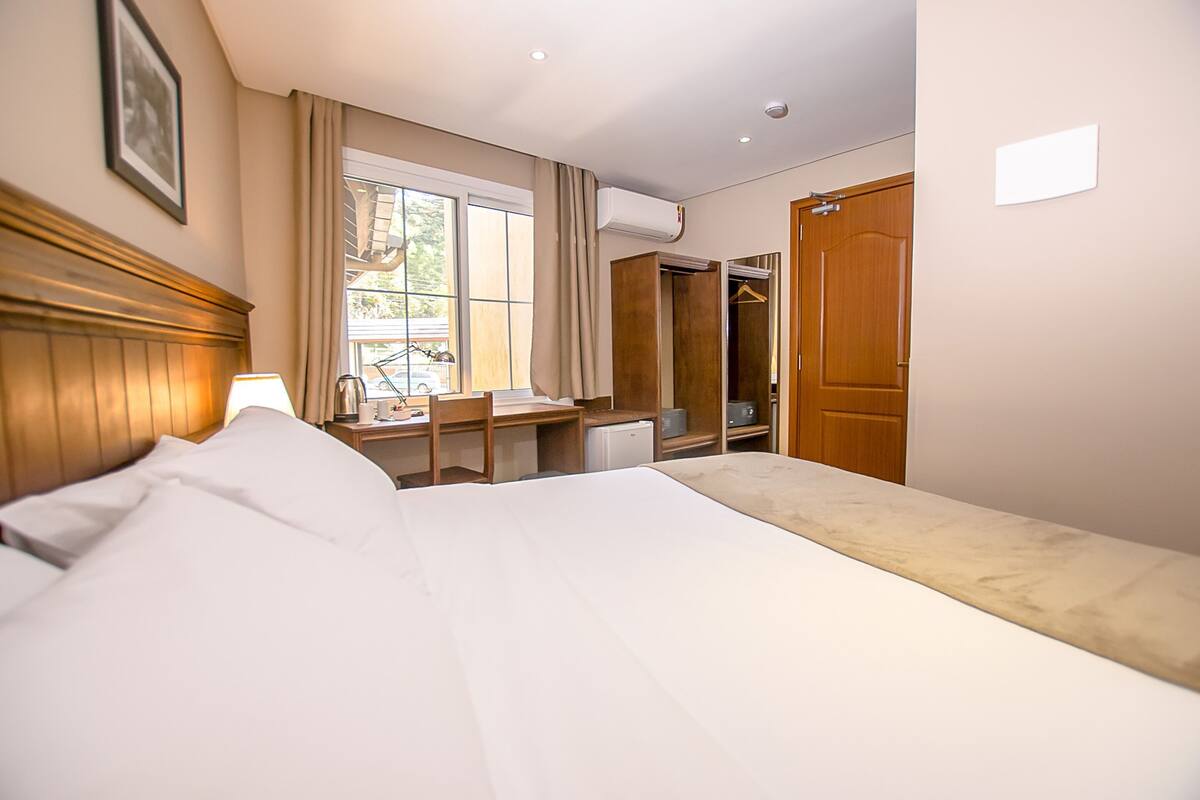A hotel room with a bed, desk, chair, and a wardrobe.