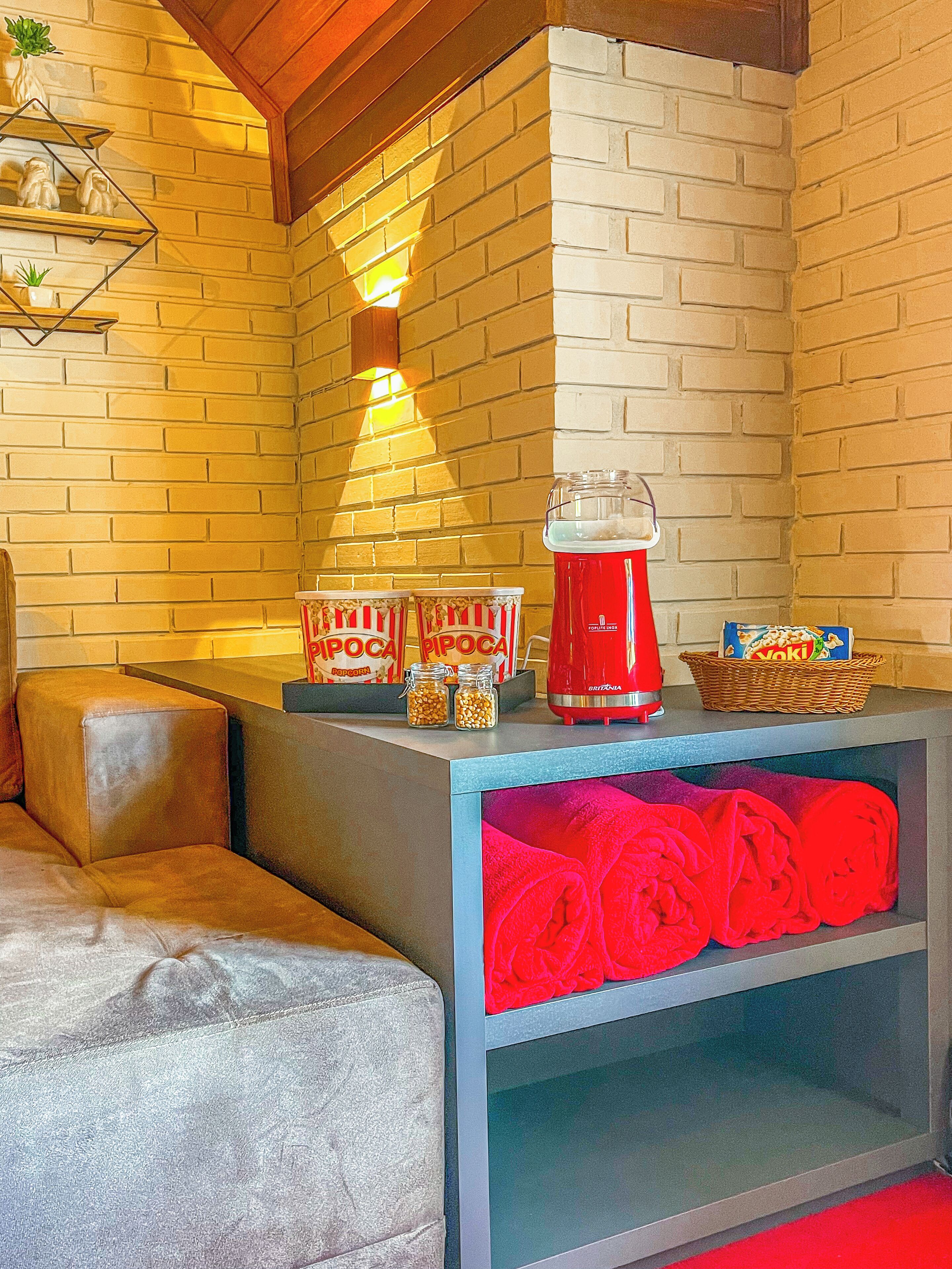 A seating area with a brick wall, a red kettle, popcorn, and a basket of snacks.