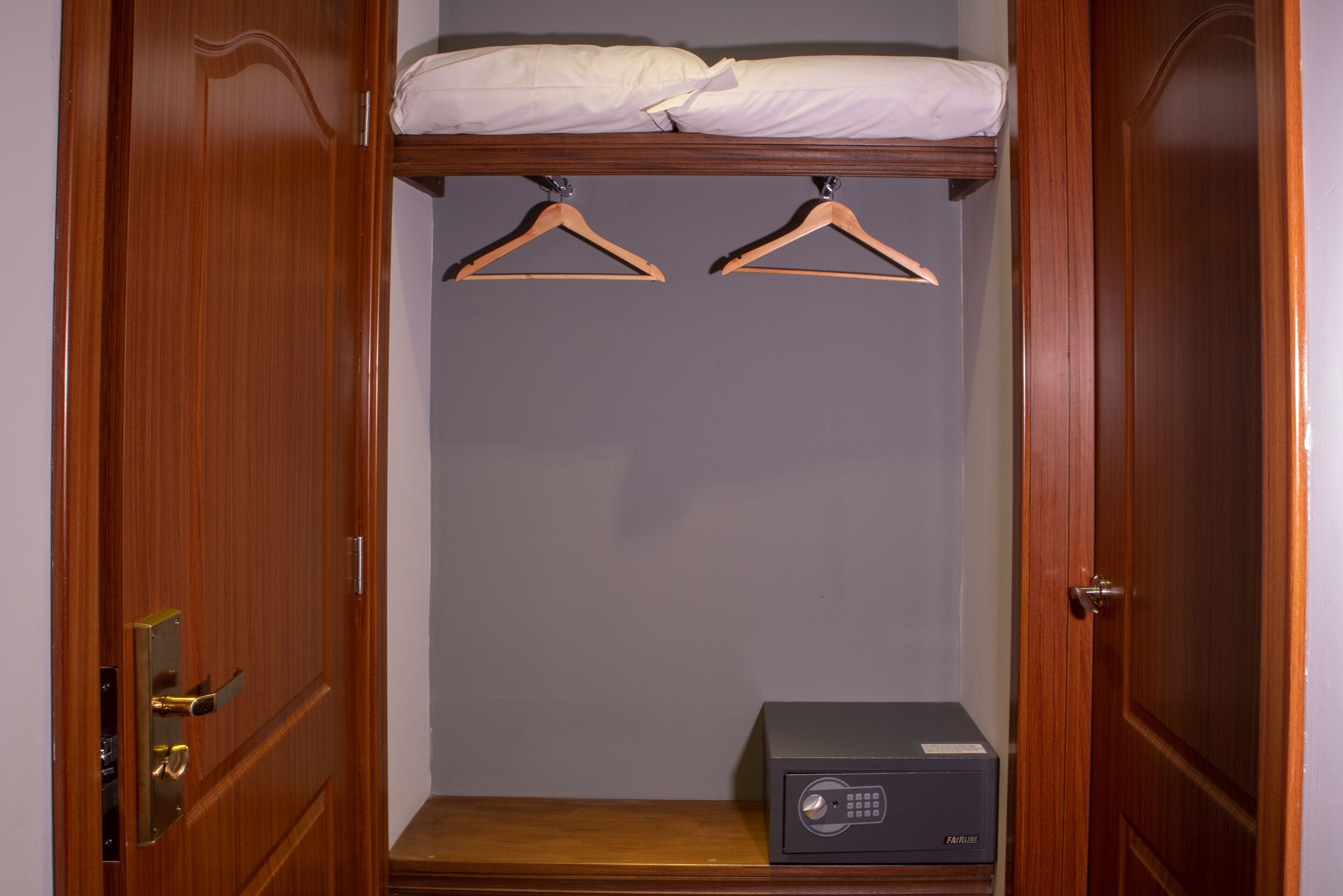 A walk-in closet with wooden doors, a bed with white bedding, two wooden hangers, and a black electronic device on the floor.