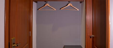 A walk-in closet with wooden doors, a bed with white bedding, two wooden hangers, and a black electronic device on the floor.