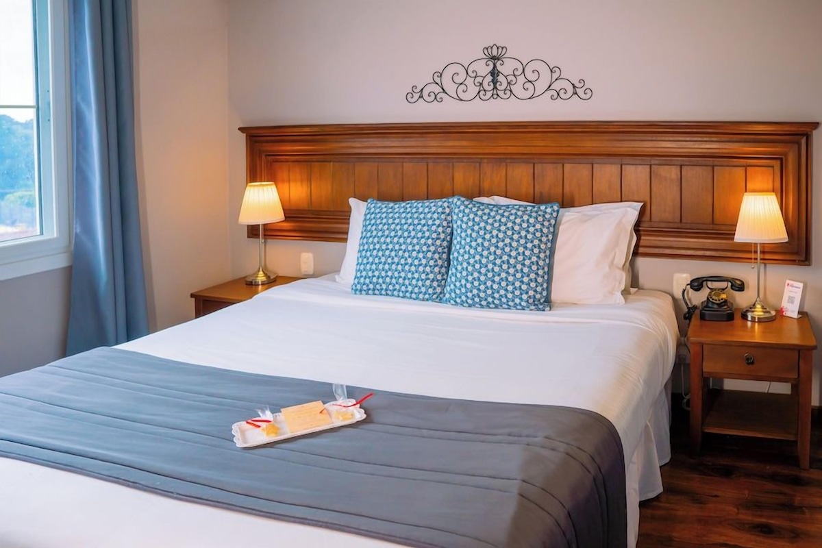 A hotel room with a large bed, two bedside tables, a decorative wall piece, and a tray with breakfast items.
