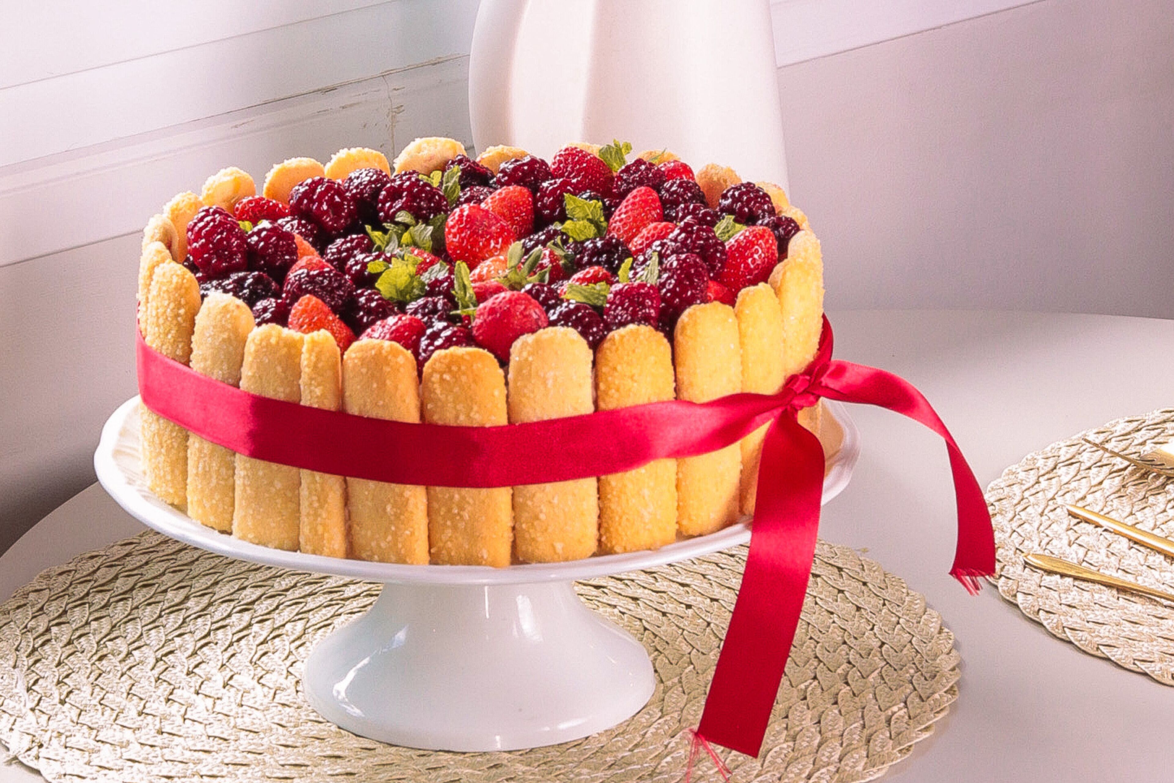A cake with a red ribbon on a white stand.