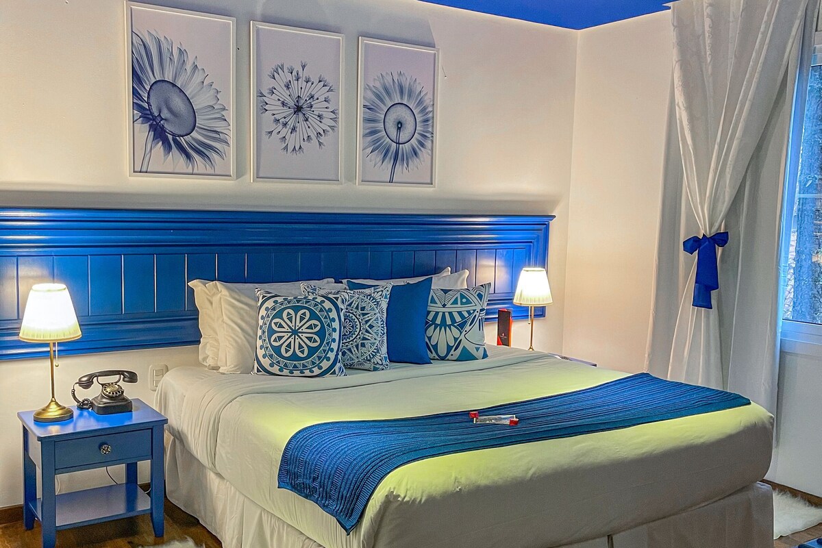 A bedroom with a bed, bedside lamps, a nightstand, and wall art.