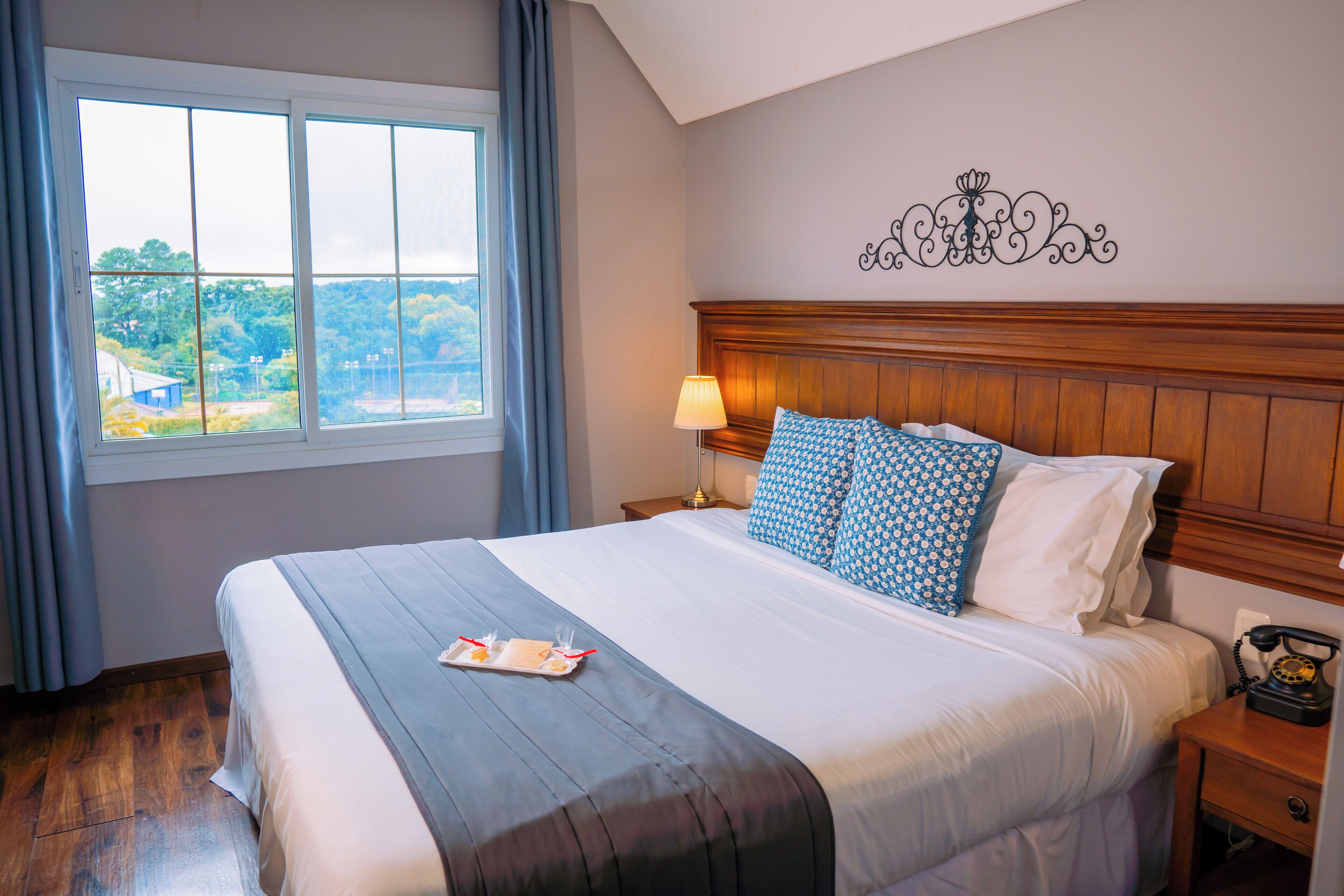 A neatly made bed with a tray of breakfast items, a bedside lamp, and a telephone on a wooden nightstand.