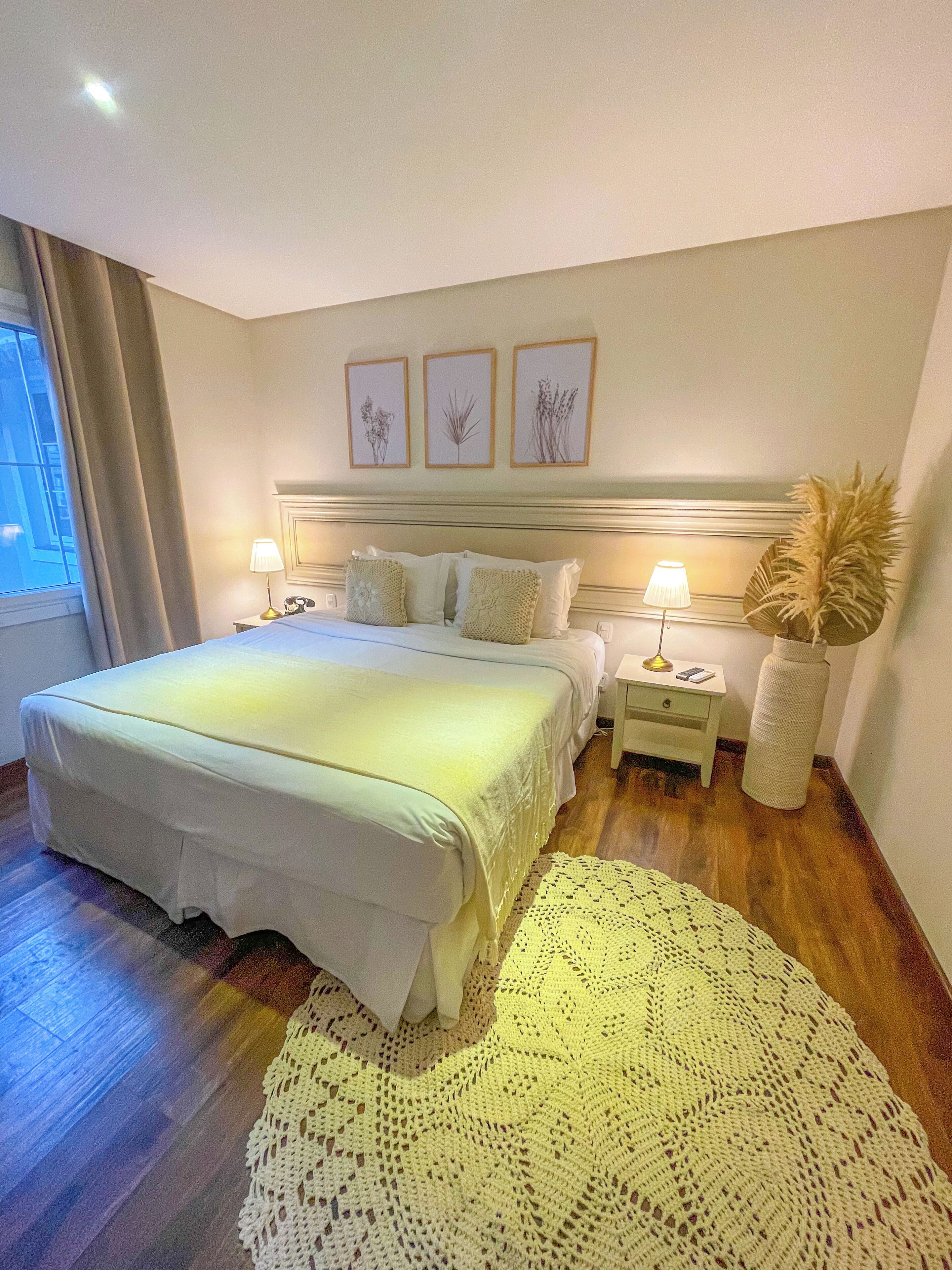Une chambre à coucher bien aménagée, avec un grand lit, des lampes de chevet, une plante décorative et des œuvres d’art botanique encadrées accrochées au mur.