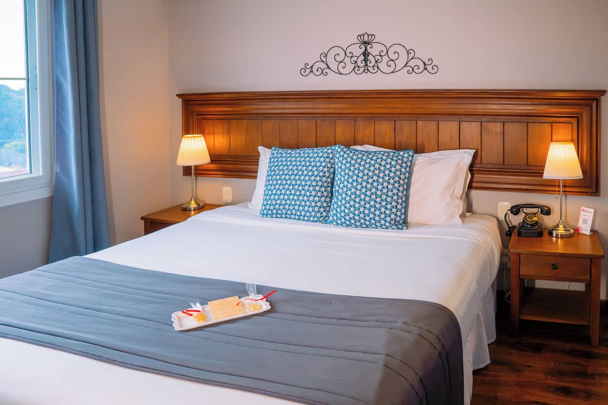A neatly made bed with a tray of breakfast items, two bedside lamps, a telephone, and a decorative wall piece.