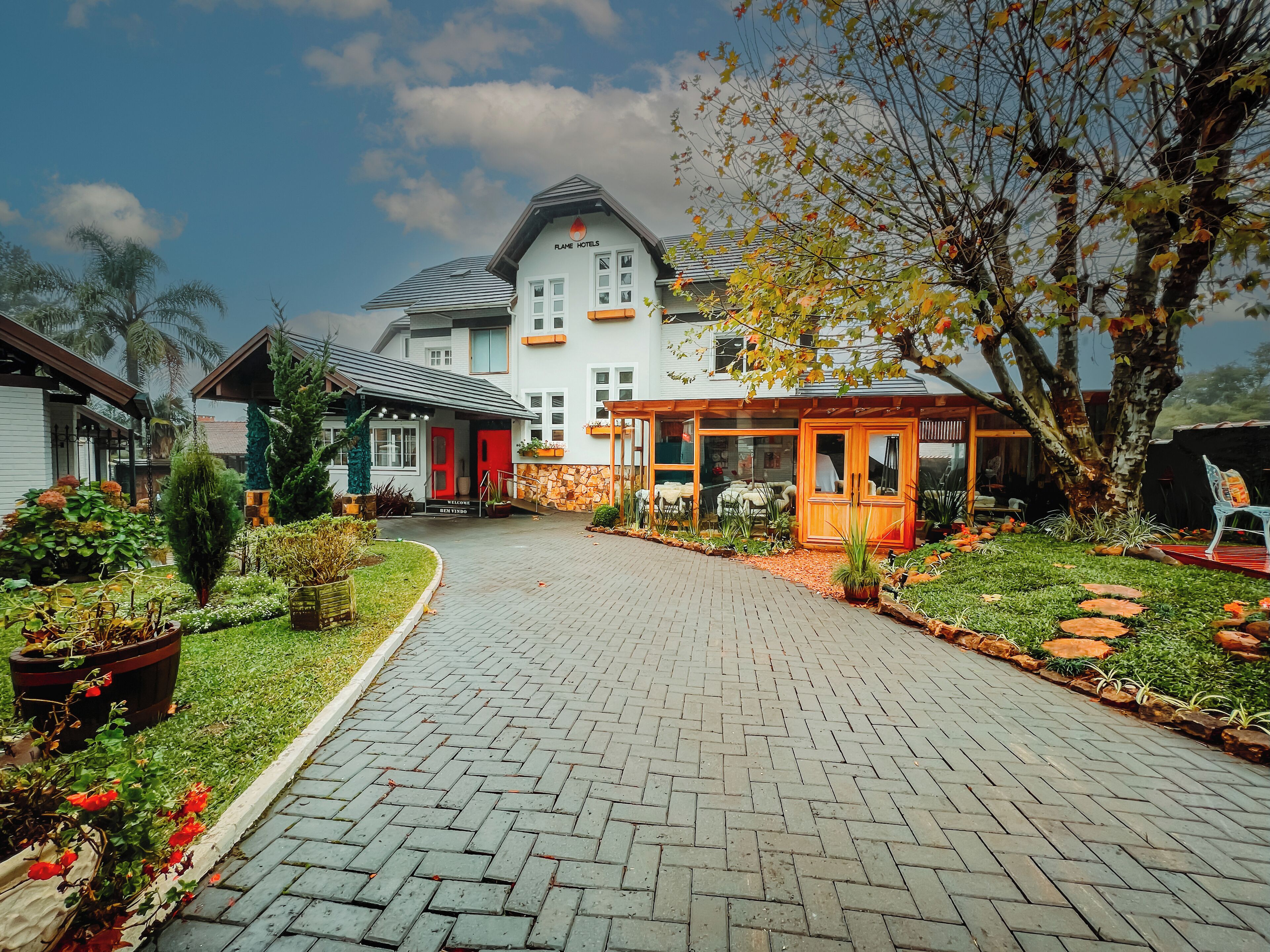 A hotel with a paved driveway leading to a covered entrance, surrounded by well-maintained gardens and a variety of plants.