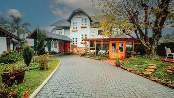 A hotel with a paved driveway leading to a covered entrance, surrounded by well-maintained gardens and a variety of plants.