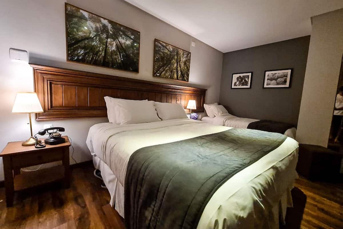 A hotel room with a large bed, wooden headboard, two bedside tables with lamps, and artwork on the walls.