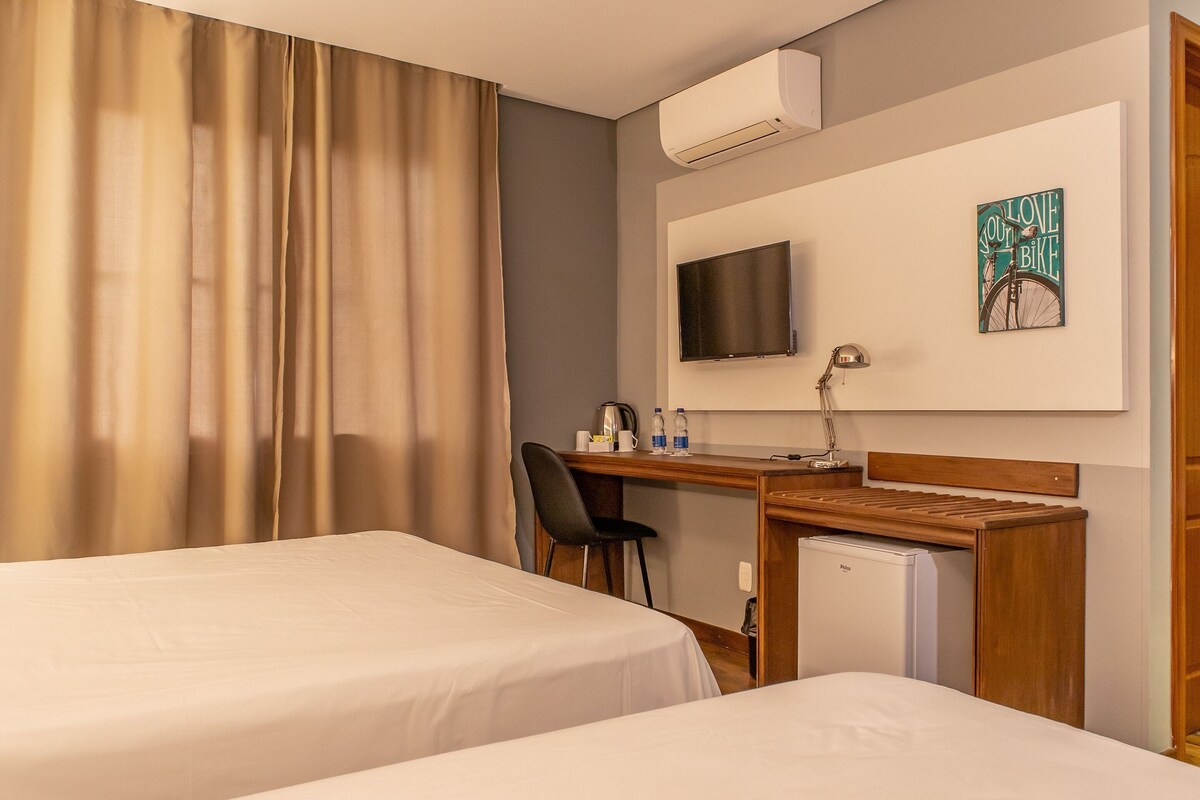 Una habitación de hotel con dos camas, un escritorio con una silla, un televisor y un aire acondicionado.