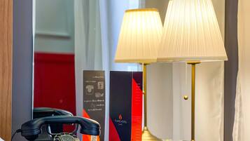 Een hotelkamer met een nachtkastje waarop een telefoon, een lamp en een brochure staan.