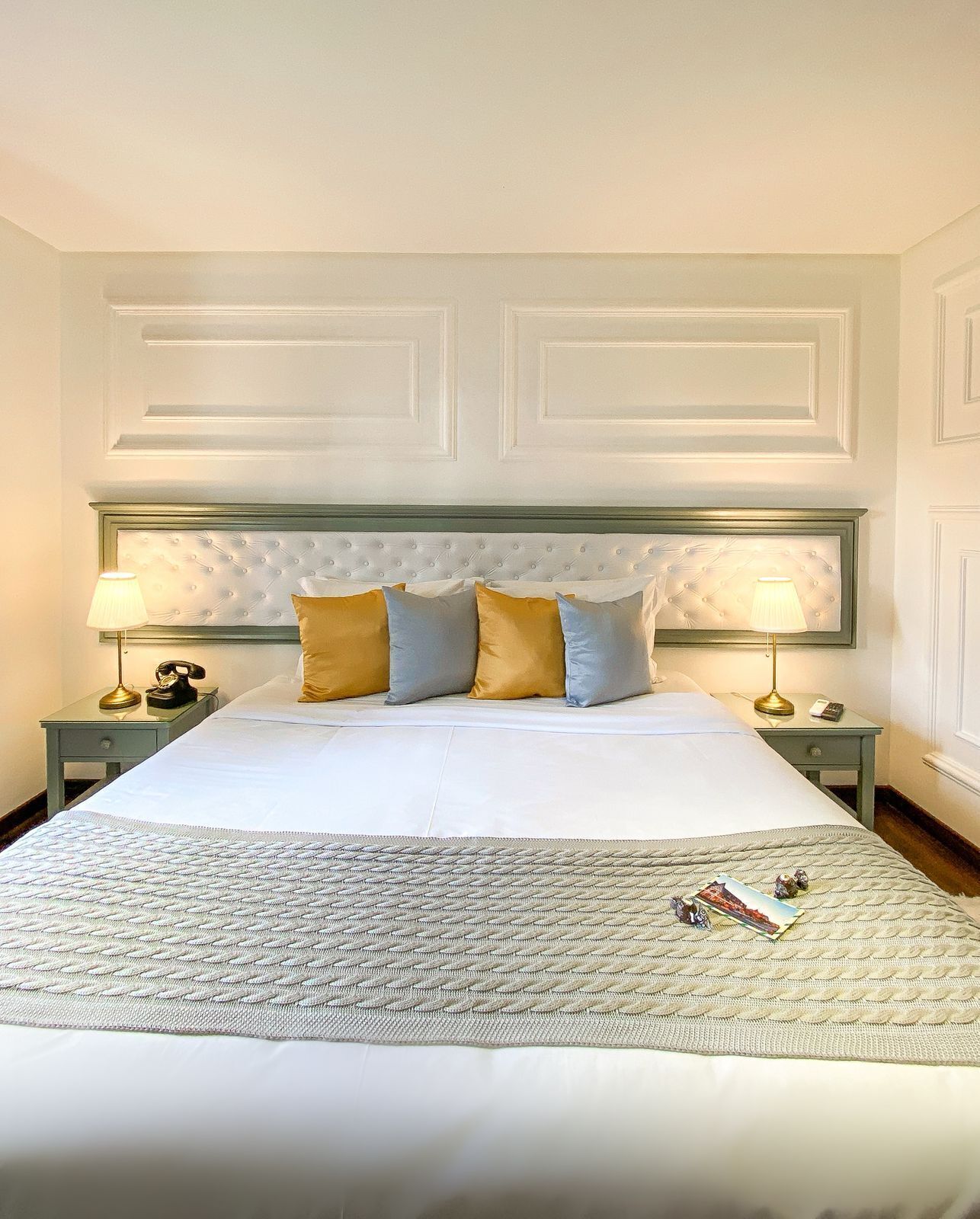 A neatly made bed with a tufted headboard, two bedside tables with lamps, and a patterned throw blanket.