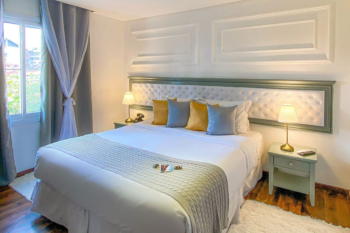 A neatly arranged bedroom with a large bed, two bedside tables, and a window with curtains.