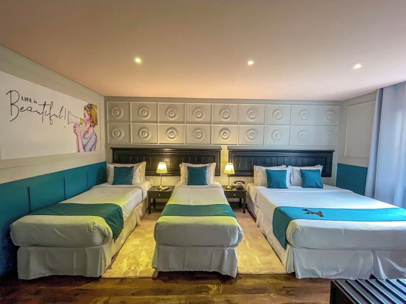A hotel room with three single beds, a large mirror, and a decorative wall with a motivational quote.