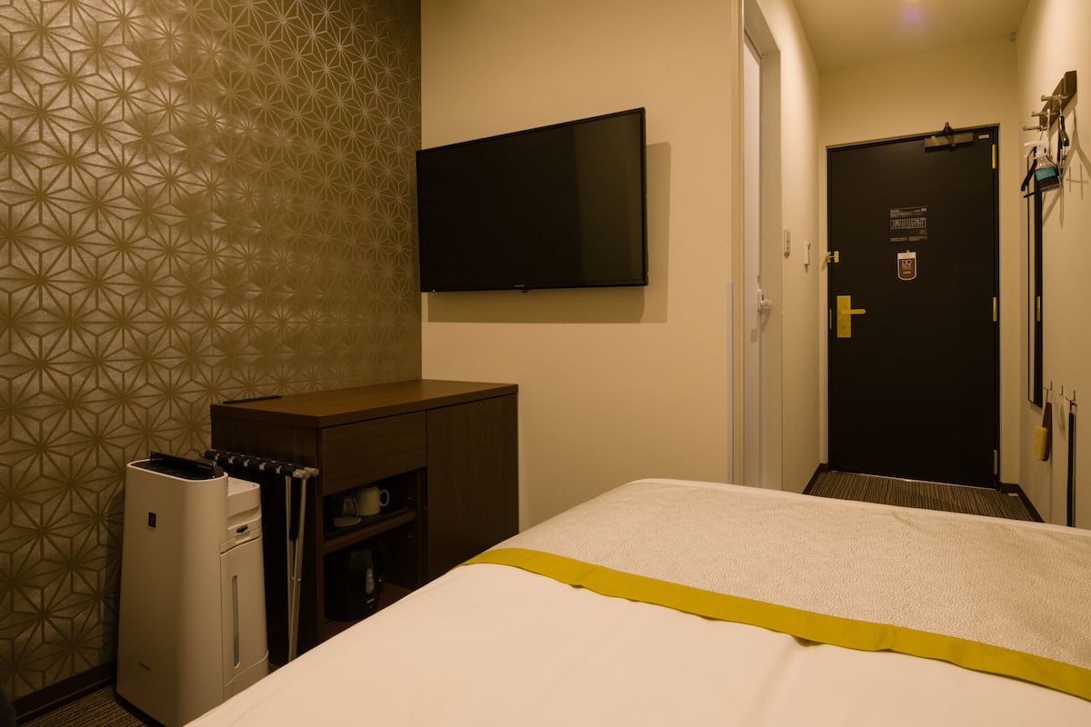 A hotel room with a bed, a TV mounted on the wall, a minibar, and a door with a lock.