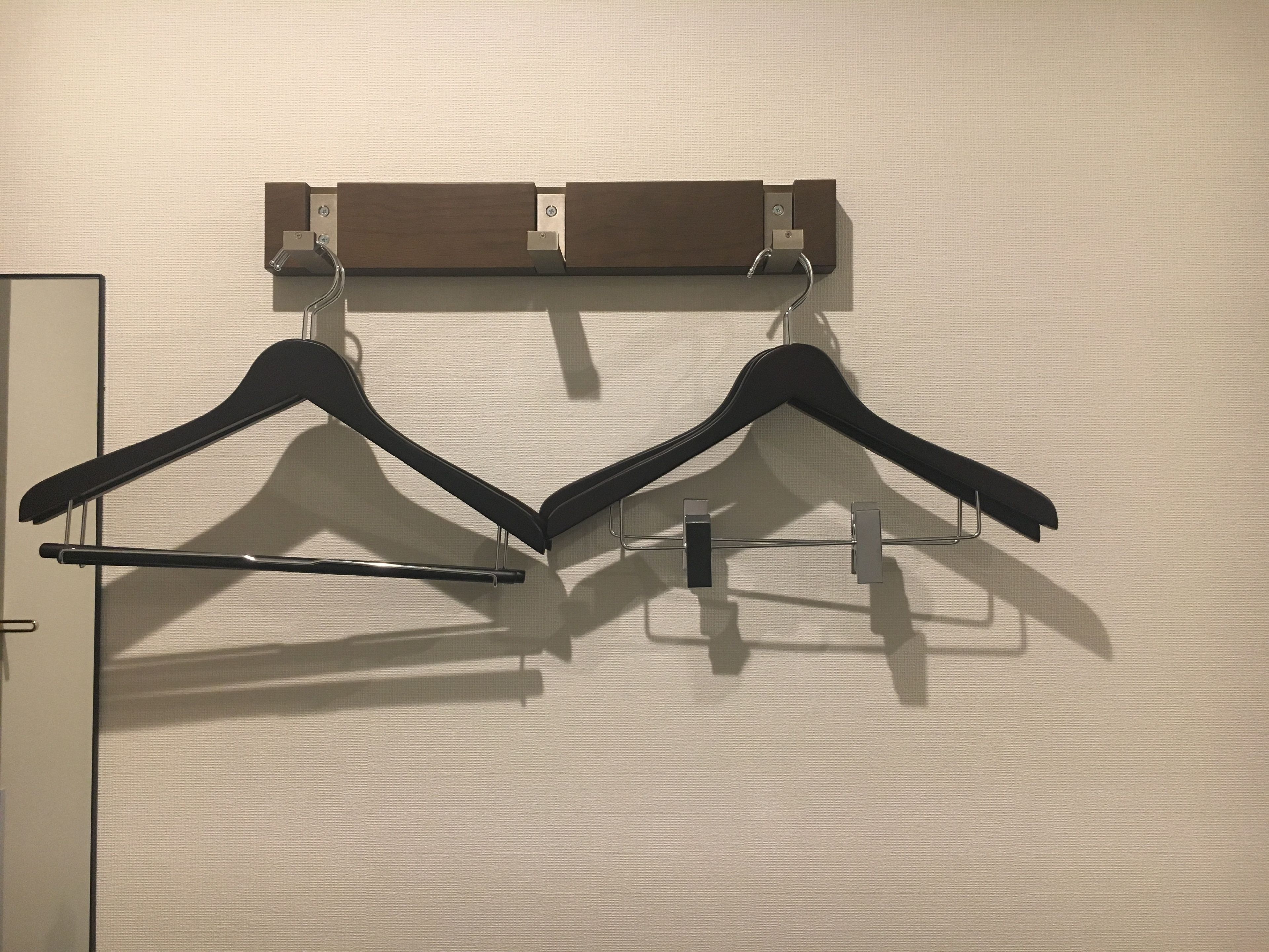 A wall-mounted clothes rack with two black hangers and a wooden panel above it.