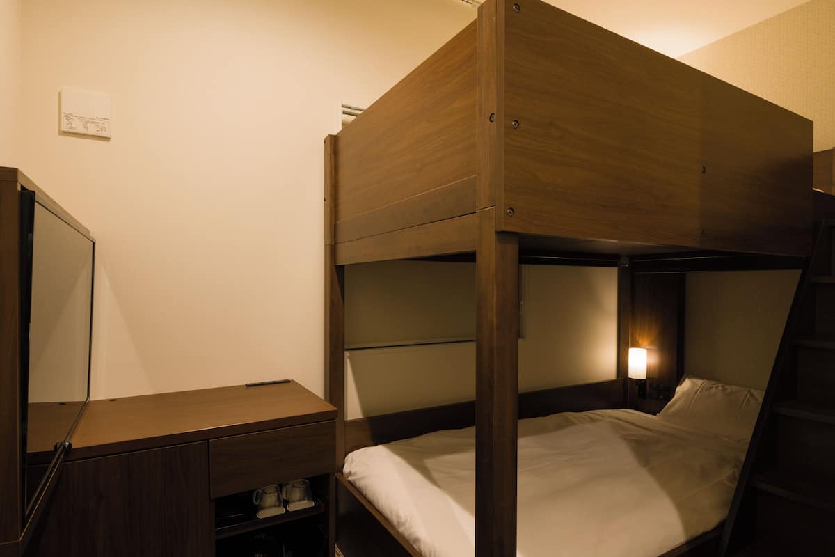 A bunk bed with a wooden frame, a bedside table, and a lamp.