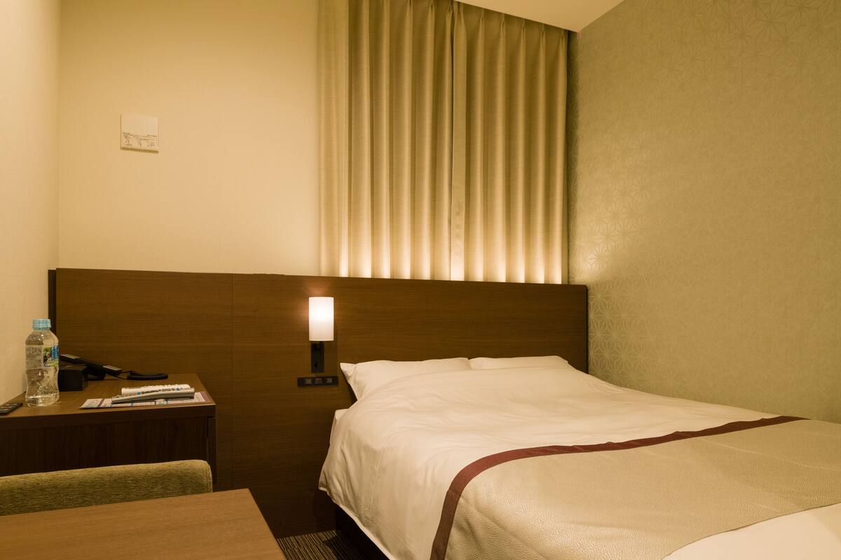 A hotel room with a bed, a desk, a lamp, and a window with curtains.