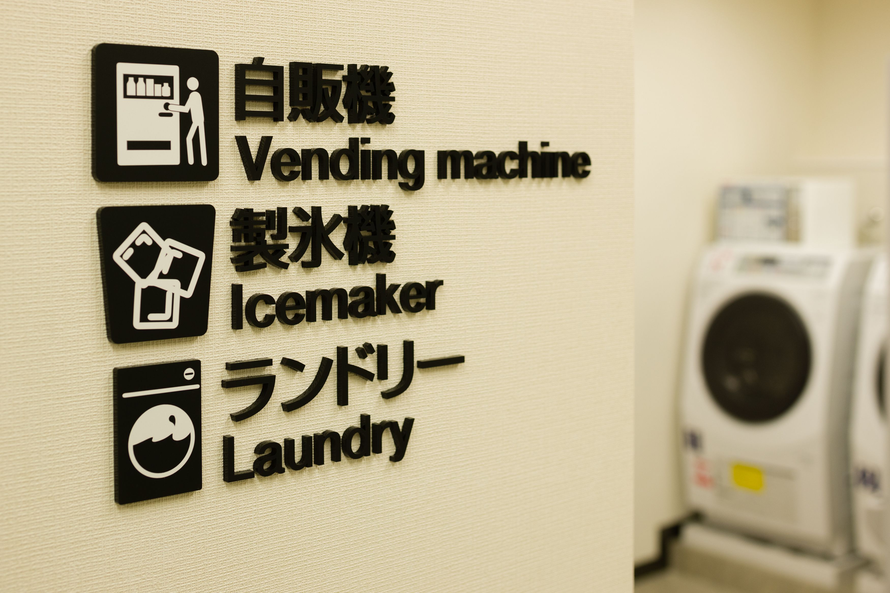 A wall with signs for a vending machine, ice maker, and laundry.