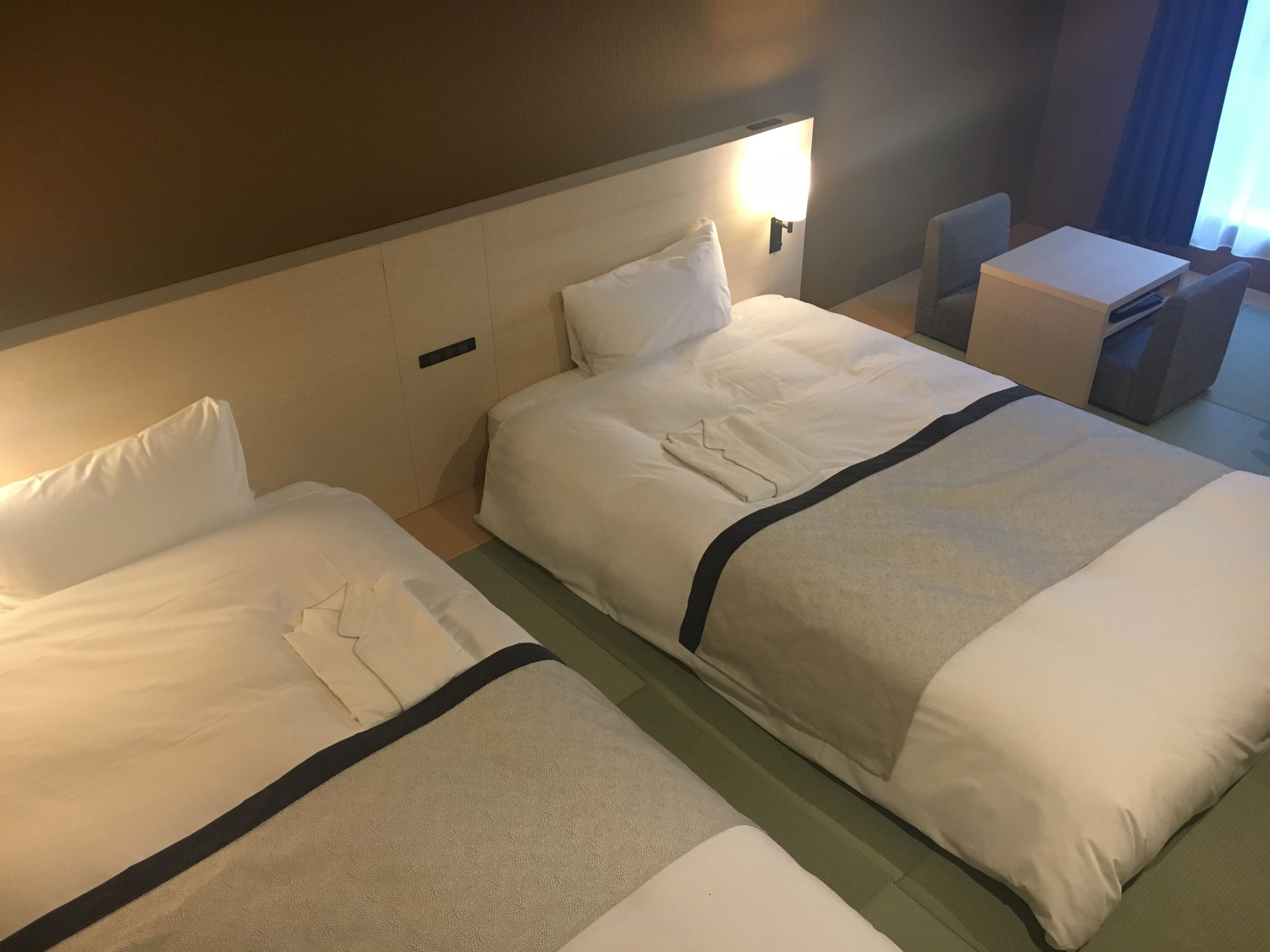 Habitación de hotel con dos camas, una mesita pequeña y una silla.