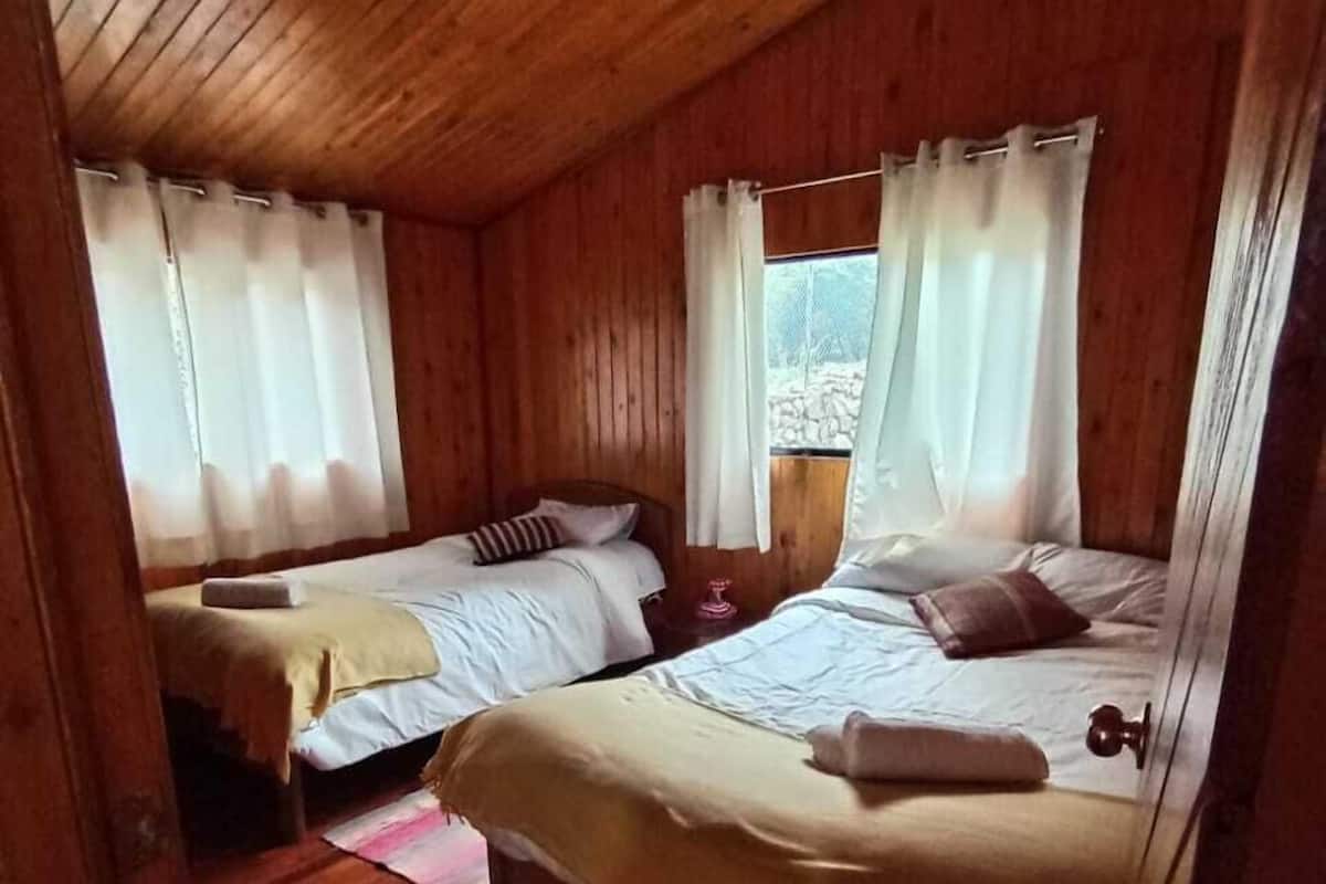 Ein Zimmer in einer Holzhütte mit zwei Betten, jeweils mit Kissen und Decke.