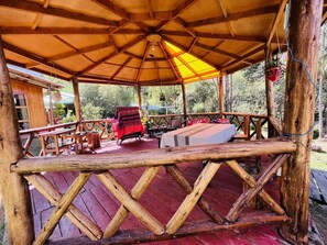 A wooden deck with a covered seating area, tables, and chairs. - Ecolodge Las Cabañas en Urubamba (Urubamba)