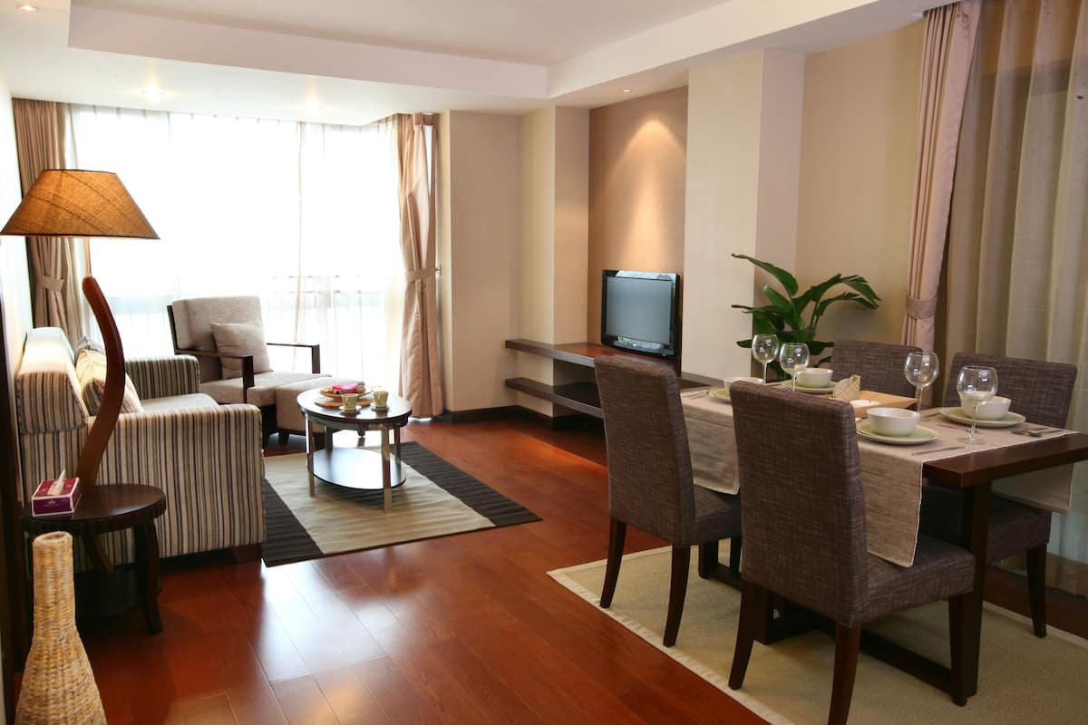 A modern living room with a sofa, armchairs, a coffee table, a TV, and a dining area with a table set for two.