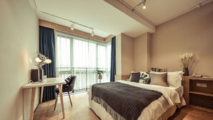 A modern hotel room with a wooden floor, a desk with a lamp, a bed with a patterned blanket, and a nightstand with a vase of flowers. - Shanghai Annshe Hotel (Shanghai)