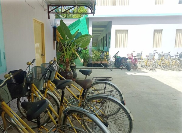 Une cour où sont garés des vélos devant un bâtiment doté d’un auvent vert et de plantes en pot.