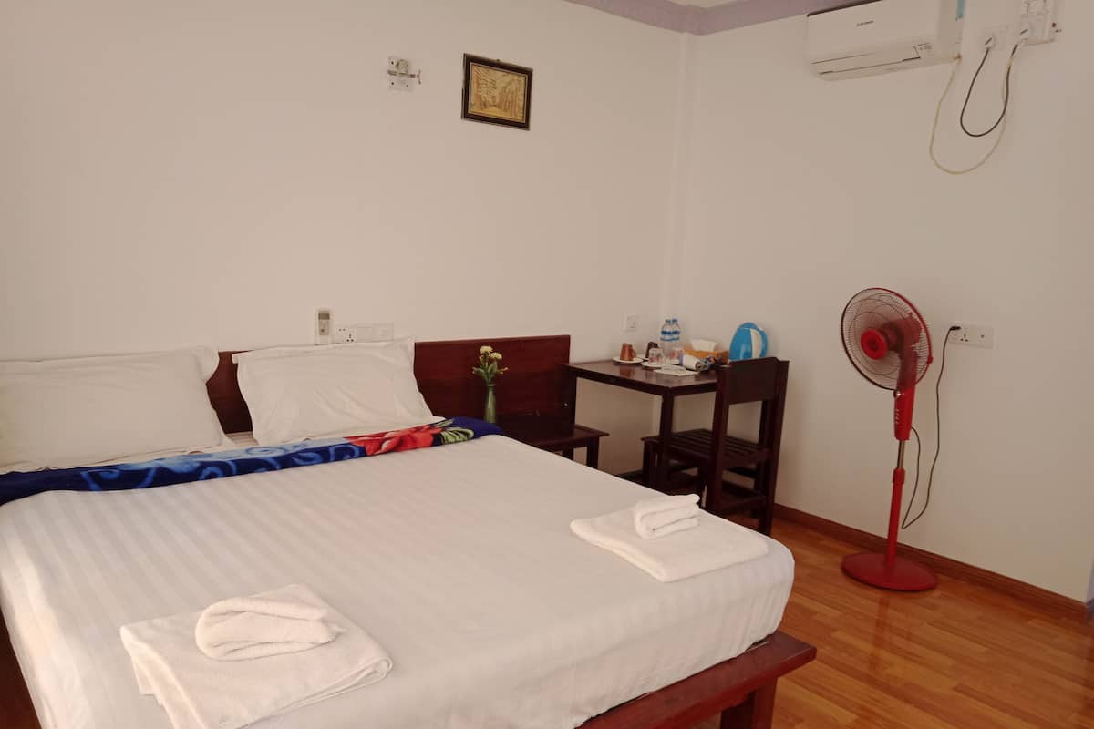 Une chambre d’hôtel équipée d’un lit, d’une table de chevet, d’une chaise et d’un ventilateur sur pied.