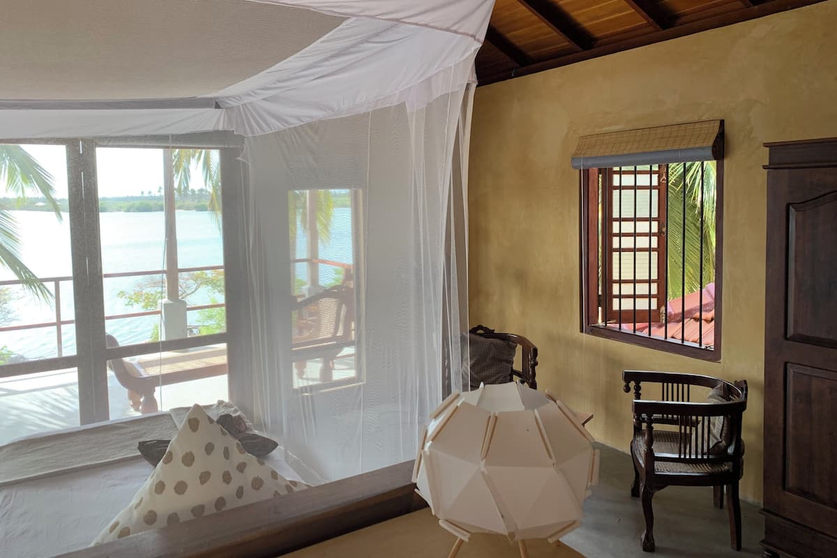 Una habitación con un ventanal grande que da a una masa de agua, techo de madera y una silla cerca de la ventana.