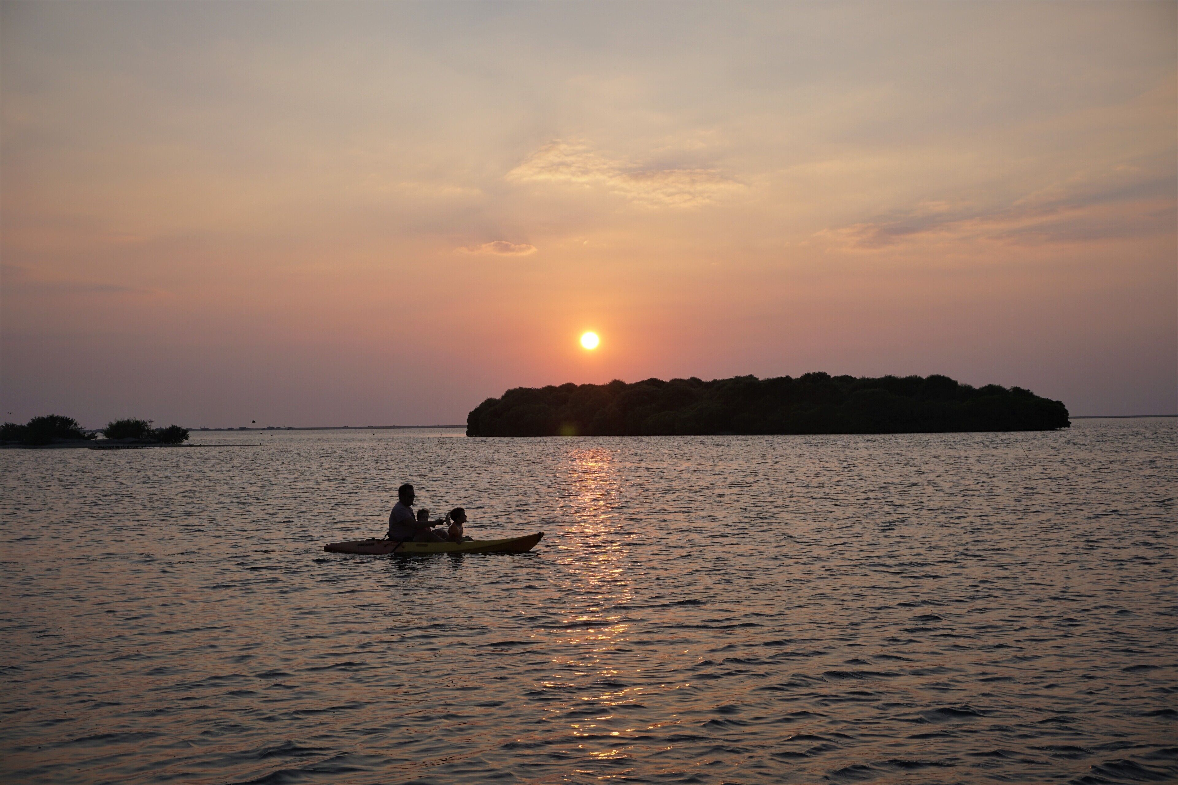 A sunset over a calm body of water with a small island in the distance.