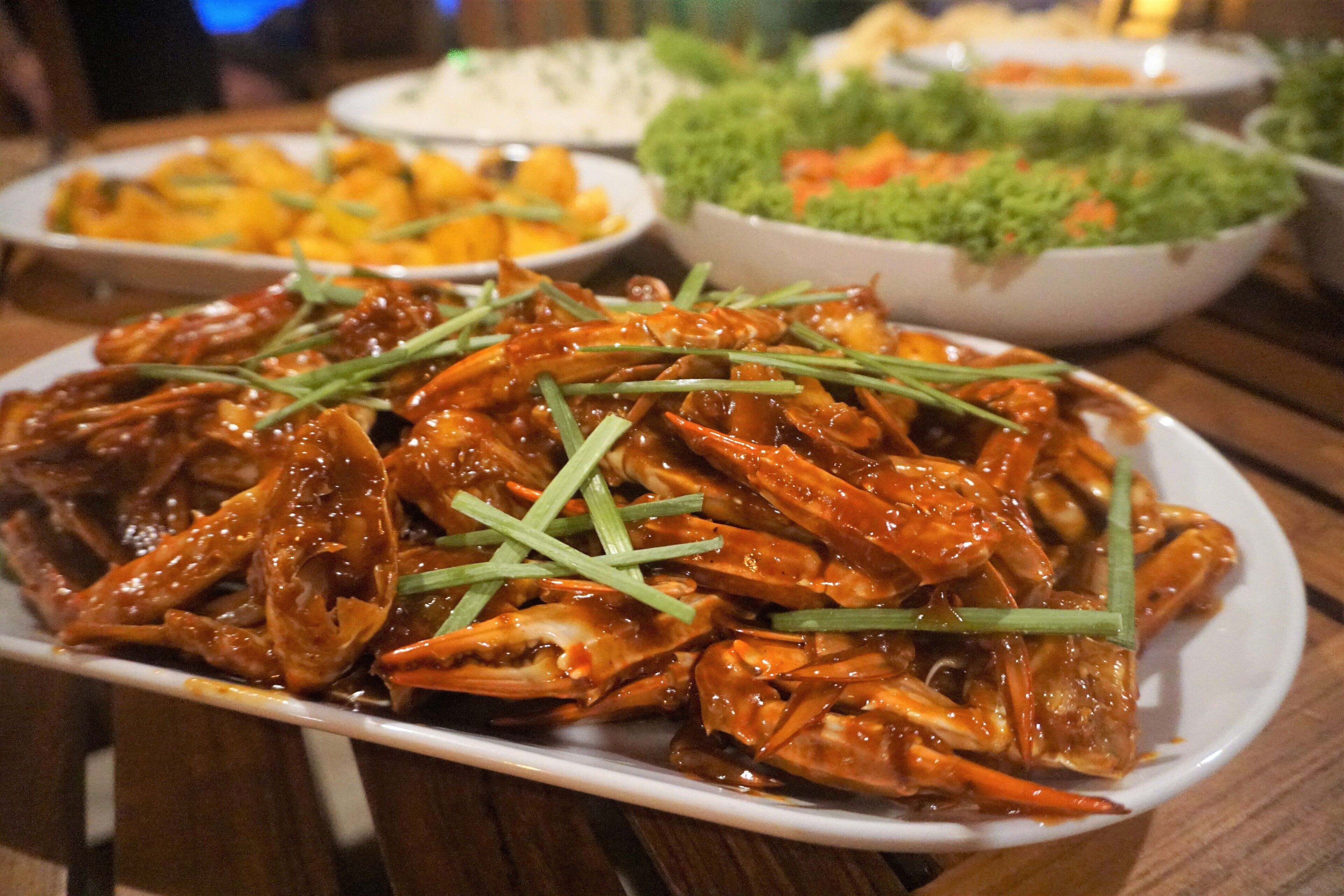 Un plato de cangrejo picante con guarnición verde sobre una mesa de madera.