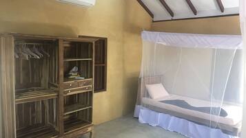 A room with a wooden wardrobe, a bed with a mosquito net, and an air conditioning unit on the wall.