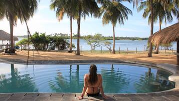 A woman sitting by a pool with a view of the water and palm trees.