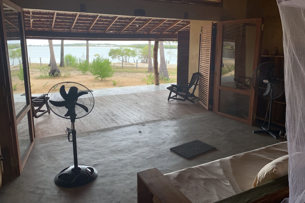 Una habitación con vistas a la playa, un ventilador, una silla y una cama.