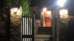Una escalera de piedra que lleva a una puerta de madera, iluminada por dos luces a cada lado, en la noche.