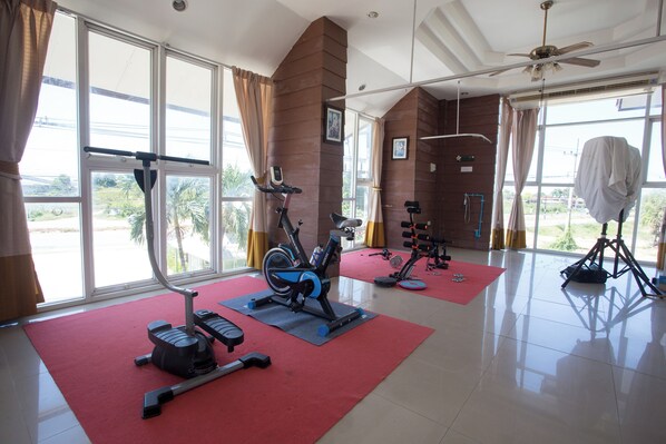 Un gimnasio amplio con diverso equipo de ejercicio, ventanas grandes y un ventilador de techo.