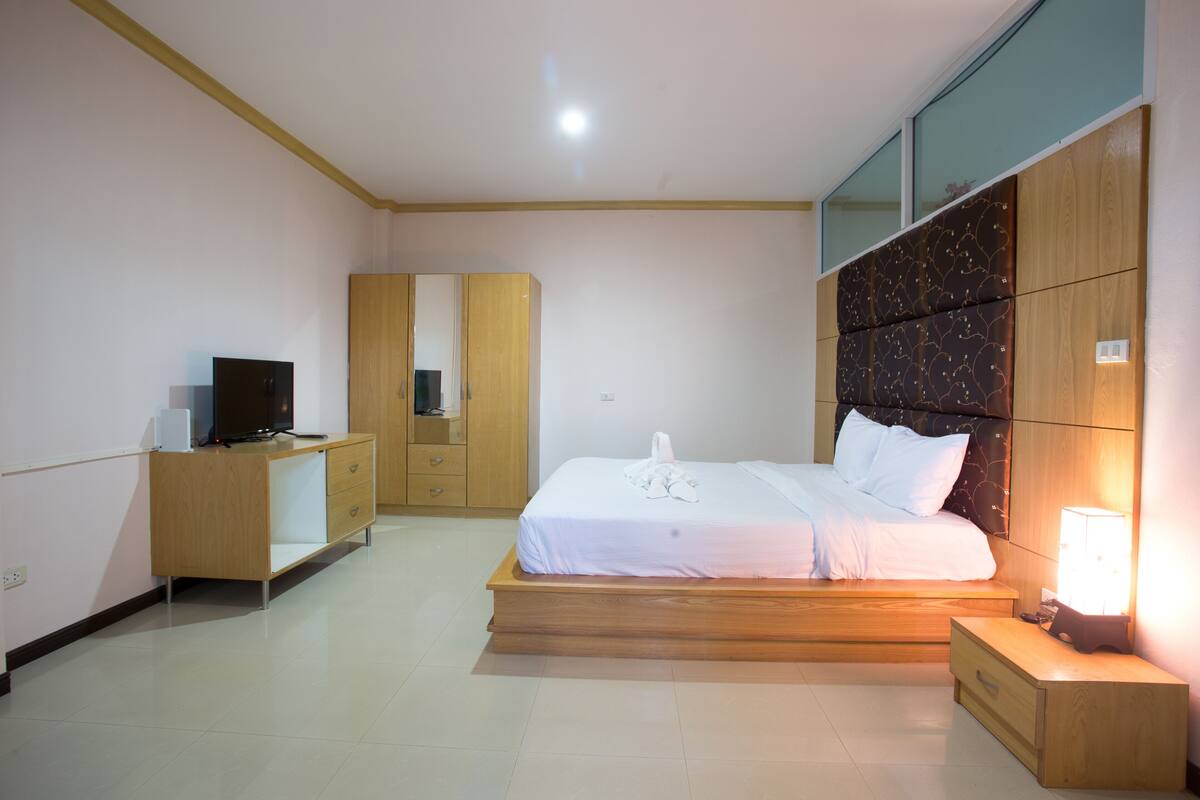 A modern bedroom with a wooden bed, a nightstand, a TV on a wooden dresser, and a wardrobe.