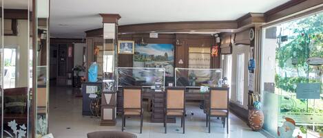 A spacious hotel lobby with a dining area, multiple seating options, and a large window offering a view of the outdoors.