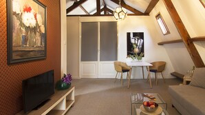 Een gezellige woonkamer met een flatscreen televisie, een glazen bijzettafeltje met appels, een bank en een eethoek met stoelen.