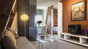 Een moderne woonkamer met een glazen salontafel, een bank, een tv op een witte dressoir en een schilderij aan de muur.