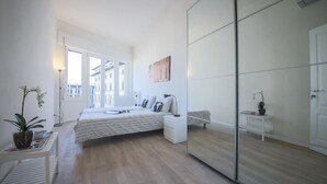 Ein modernes Schlafzimmer mit Bett, Nachttischen, einem Spiegel und einem Fenster.