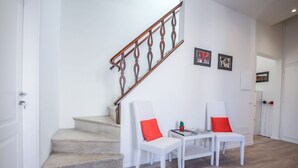 Eine Treppe mit einem Holzgeländer, eine weiße Wand mit zwei gerahmten Bildern und ein kleiner Tisch mit zwei Stühlen.