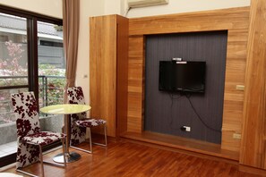 Una habitación moderna con una pared de madera decorativa, un televisor de pantalla plana montado en ella y un balcón con vistas a los cerezos en flor.