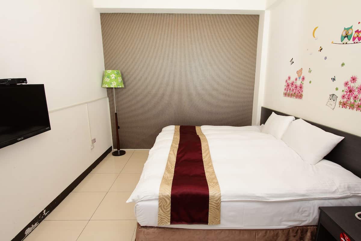 Habitación de hotel con cama, televisor montado en la pared, lámpara y pared decorada con pegatinas.