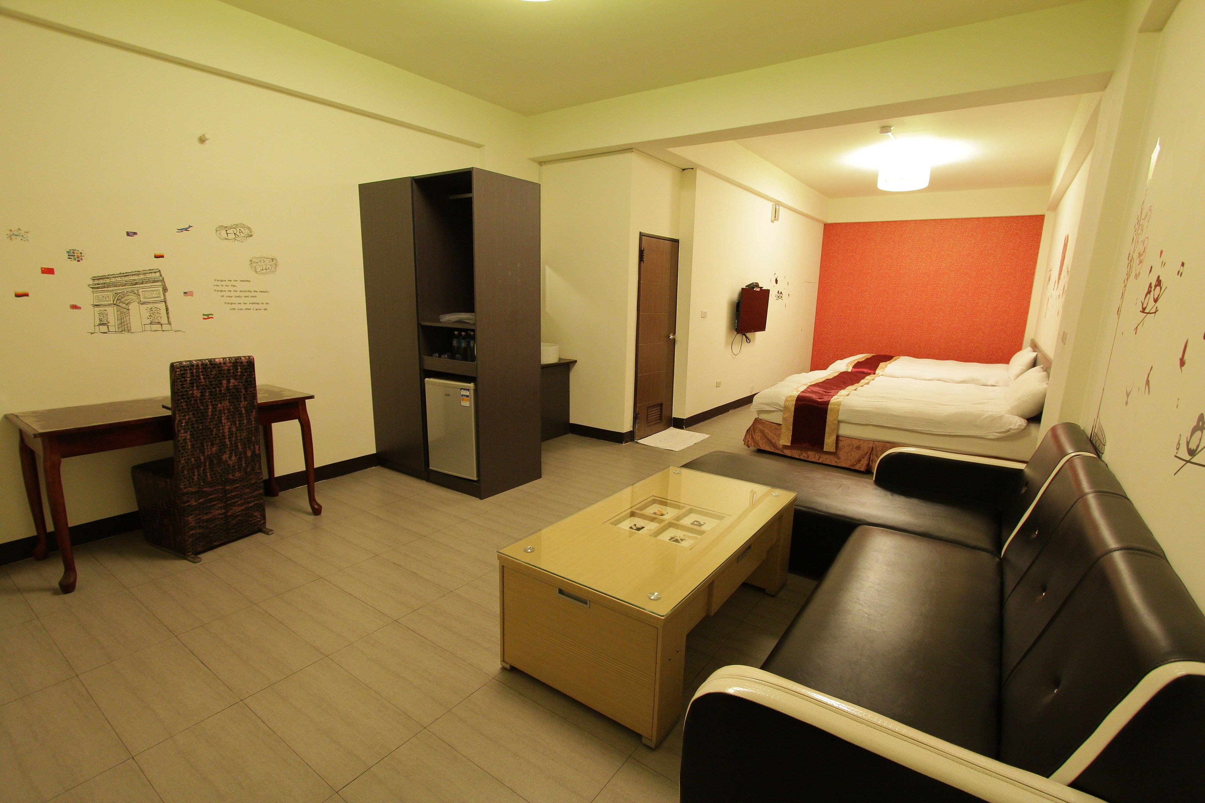 A compact hotel room with a bed, a sofa, a desk, and a small kitchenette.